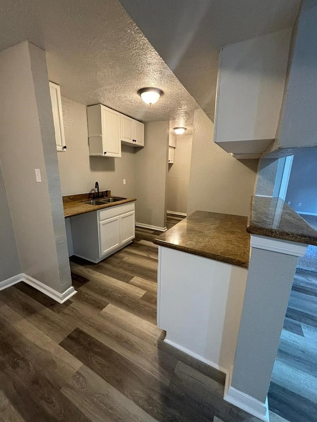 kitchen with sink, dark wood-type flooring, a textured ceiling, white cabinets, and kitchen peninsula