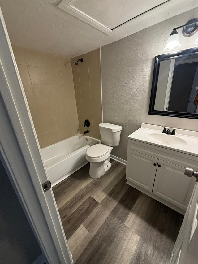 full bathroom featuring hardwood / wood-style floors, tiled shower / bath combo, vanity, toilet, and a textured ceiling