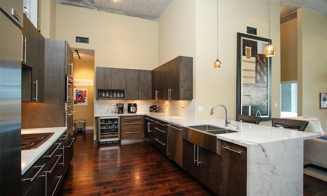 kitchen featuring appliances with stainless steel finishes, sink, wine cooler, hanging light fixtures, and a high ceiling