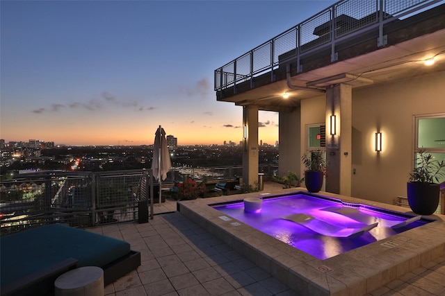 pool at dusk with a patio and an in ground hot tub