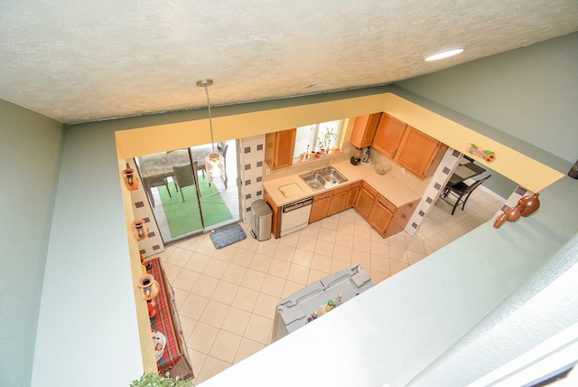 kitchen with light tile patterned floors, sink, hanging light fixtures, white dishwasher, and a textured ceiling