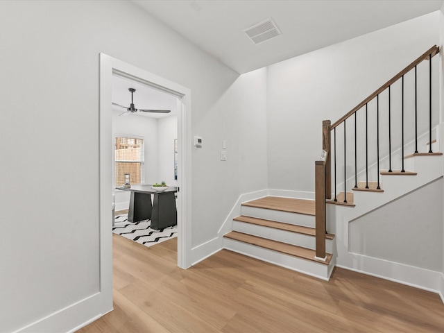 stairway featuring a ceiling fan, baseboards, visible vents, and wood finished floors