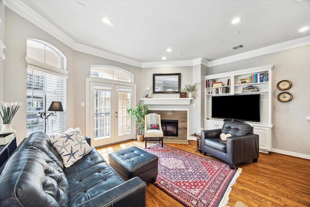 living room featuring wood-type flooring, crown molding, a fireplace, and french doors