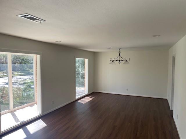 unfurnished room featuring dark wood-type flooring, a chandelier, and a healthy amount of sunlight