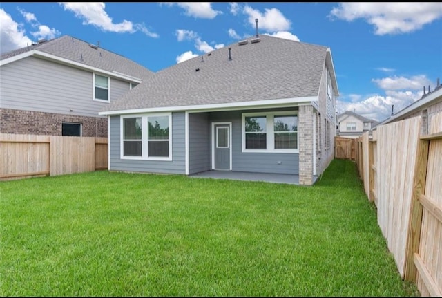 rear view of property featuring a lawn, roof with shingles, a patio area, and a fenced backyard