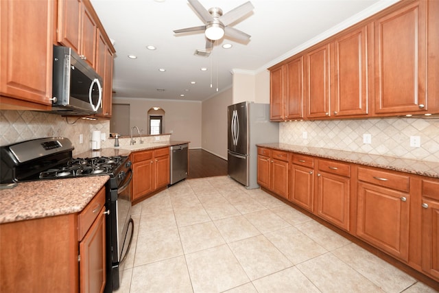 kitchen with sink, crown molding, light tile patterned floors, appliances with stainless steel finishes, and light stone countertops