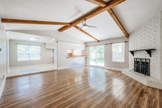 unfurnished living room featuring a healthy amount of sunlight, wood-type flooring, a fireplace, and vaulted ceiling with beams