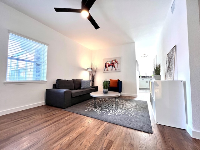 living room with a ceiling fan, visible vents, baseboards, and wood finished floors