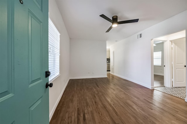 empty room featuring ceiling fan, visible vents, baseboards, and dark wood-style flooring