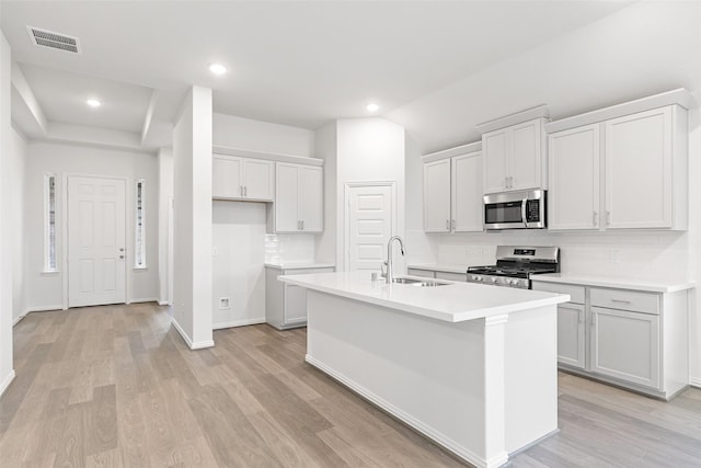 5830 Westwood Shore Dr, Katy, TX 77493 - kitchen featuring appliances with stainless steel finishes, a sink, a center island with sink, light wood finished floors, and recessed lighting