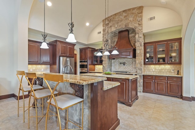 kitchen with vaulted ceiling, appliances with stainless steel finishes, hanging light fixtures, custom exhaust hood, and a kitchen island with sink