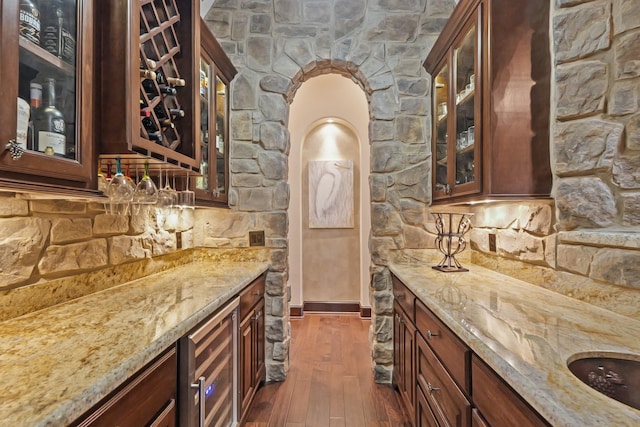 bar with dark hardwood / wood-style flooring, light stone countertops, and beverage cooler