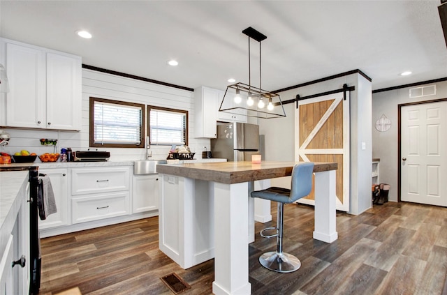 kitchen with stainless steel refrigerator, white cabinetry, a barn door, and a center island