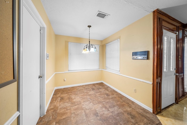 unfurnished dining area featuring a textured ceiling and a chandelier