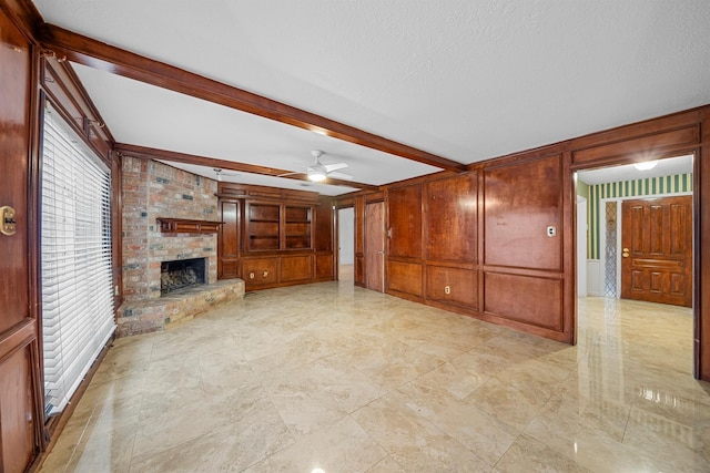 unfurnished living room with wooden walls, a fireplace, a textured ceiling, beam ceiling, and built in shelves