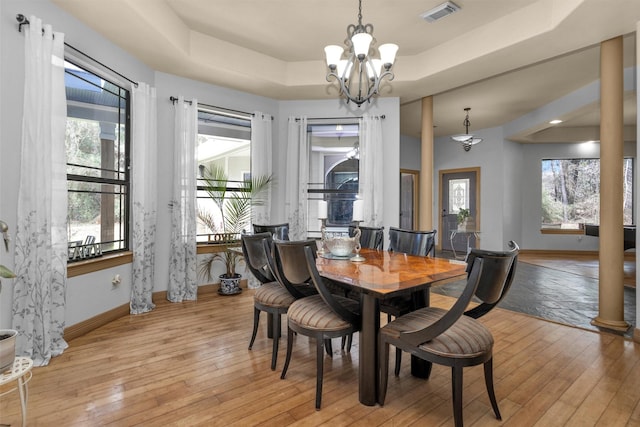 dining area featuring a tray ceiling, a notable chandelier, visible vents, light wood-style floors, and baseboards