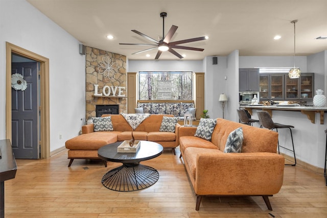 living room featuring a stone fireplace, a ceiling fan, light wood-style flooring, and recessed lighting