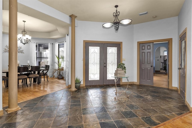 foyer featuring decorative columns, baseboards, stone tile flooring, french doors, and a chandelier