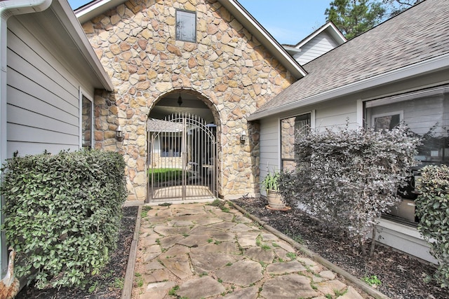 entrance to property featuring a gate and roof with shingles