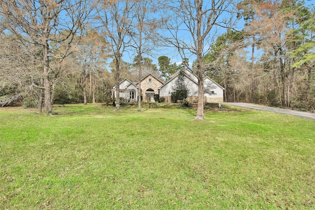 view of front of home featuring stone siding, a front yard, and driveway