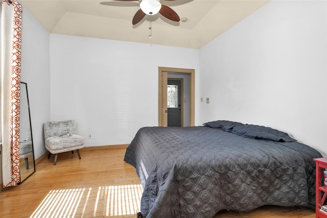 bedroom with a tray ceiling, wood finished floors, a ceiling fan, and baseboards