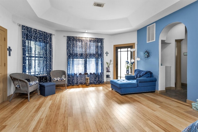 living area featuring visible vents, arched walkways, hardwood / wood-style floors, a tray ceiling, and ornate columns