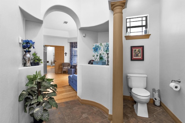 hallway featuring arched walkways, stone finish floor, visible vents, and baseboards