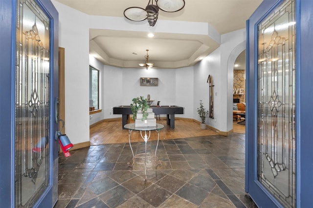 entryway with arched walkways, stone tile flooring, pool table, a raised ceiling, and baseboards