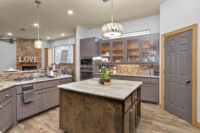 kitchen with decorative backsplash, glass insert cabinets, appliances with stainless steel finishes, a stone fireplace, and light wood-style floors