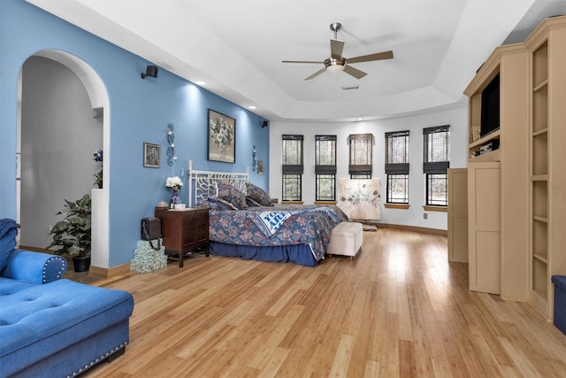 bedroom with light wood-type flooring, baseboards, arched walkways, and a tray ceiling