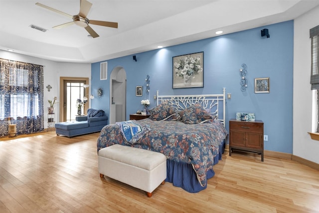 bedroom featuring baseboards, visible vents, arched walkways, wood finished floors, and a tray ceiling