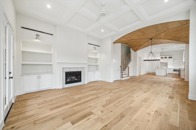 unfurnished living room featuring coffered ceiling, stairs, light wood-type flooring, built in shelves, and a fireplace