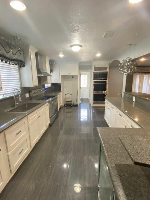 kitchen with wall chimney exhaust hood, white cabinetry, stainless steel appliances, and sink