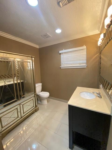 bathroom featuring crown molding, vanity, toilet, and a textured ceiling