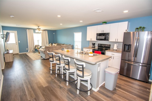 kitchen with a breakfast bar, sink, white cabinets, black appliances, and a center island with sink