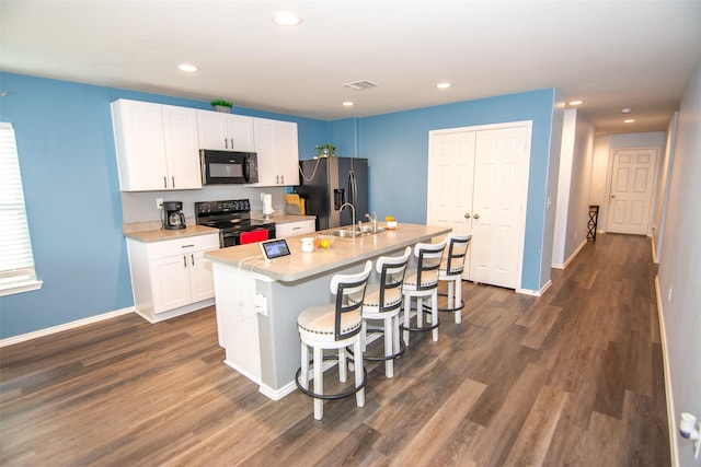 kitchen featuring white cabinetry, dark hardwood / wood-style flooring, a kitchen bar, a kitchen island with sink, and black appliances