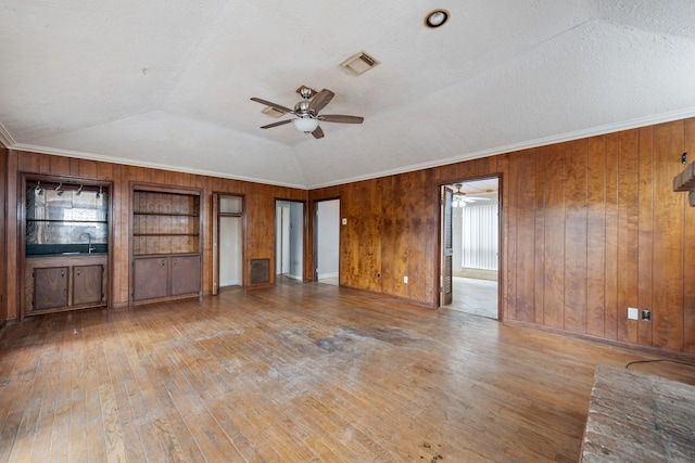 unfurnished living room with crown molding, lofted ceiling, built in shelves, and light hardwood / wood-style floors