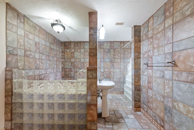 bathroom with a shower, sink, tile walls, and a textured ceiling