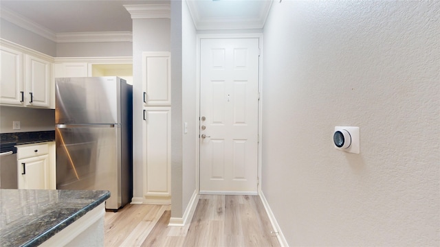 kitchen with dark stone countertops, ornamental molding, stainless steel refrigerator, and white cabinets