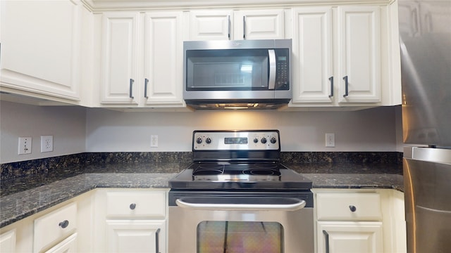 kitchen with appliances with stainless steel finishes, dark stone counters, and white cabinets