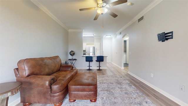 living room with crown molding, ceiling fan, and light wood-type flooring