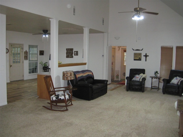 living room featuring a towering ceiling, light colored carpet, and ceiling fan