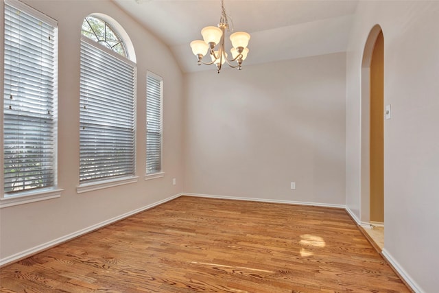 empty room featuring vaulted ceiling, a chandelier, and light wood-type flooring