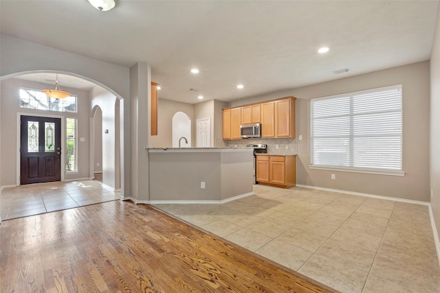 kitchen featuring appliances with stainless steel finishes, backsplash, light stone counters, kitchen peninsula, and light brown cabinets