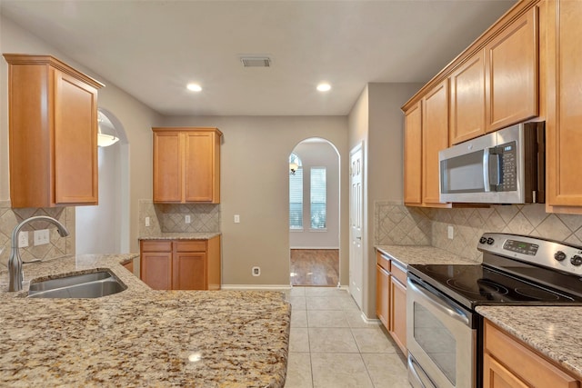 kitchen featuring light tile patterned flooring, sink, backsplash, stainless steel appliances, and light stone countertops