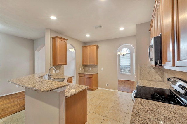 kitchen featuring sink, light stone counters, appliances with stainless steel finishes, a kitchen breakfast bar, and kitchen peninsula