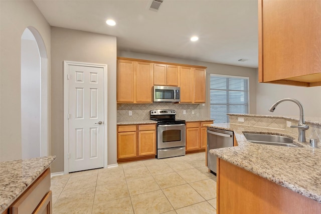 kitchen featuring appliances with stainless steel finishes, tasteful backsplash, sink, light tile patterned floors, and light stone countertops