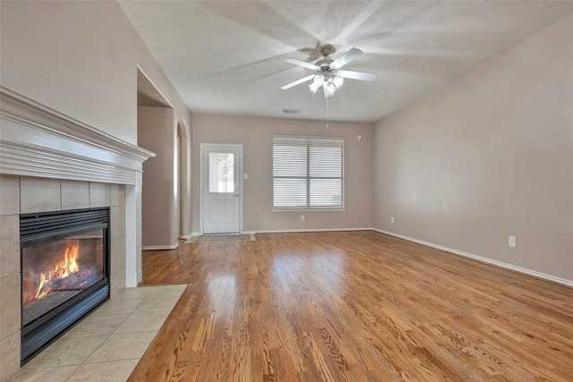 unfurnished living room with a tiled fireplace, light hardwood / wood-style floors, and ceiling fan