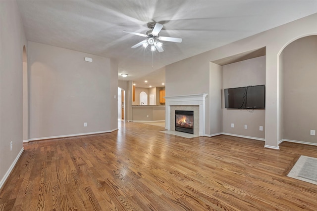 unfurnished living room with a tile fireplace, ceiling fan, and light wood-type flooring