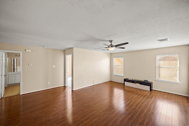 unfurnished living room with ceiling fan, a wealth of natural light, a textured ceiling, and dark hardwood / wood-style flooring